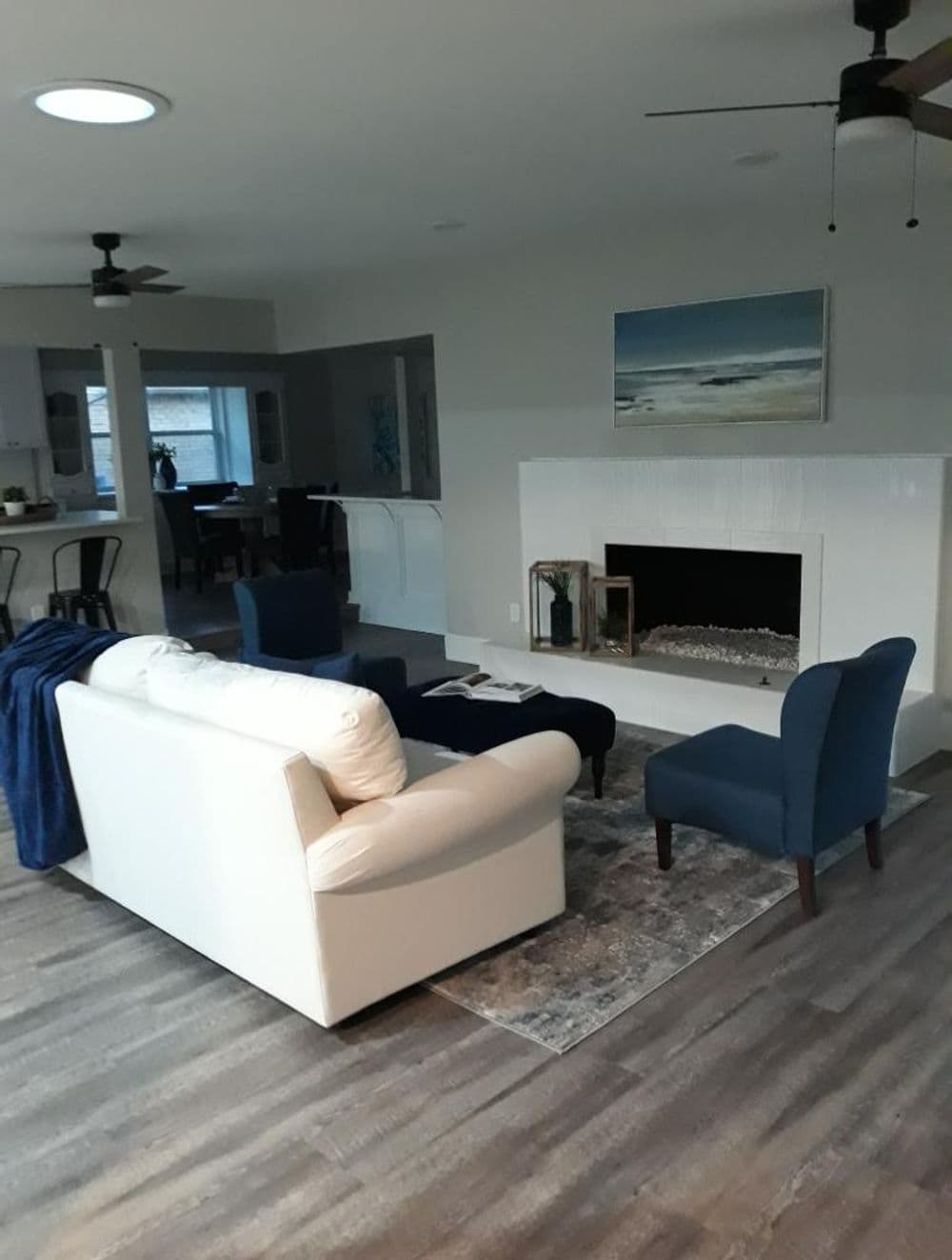 Modern living room with white sofa, armchairs, and a cozy fireplace on wood flooring.