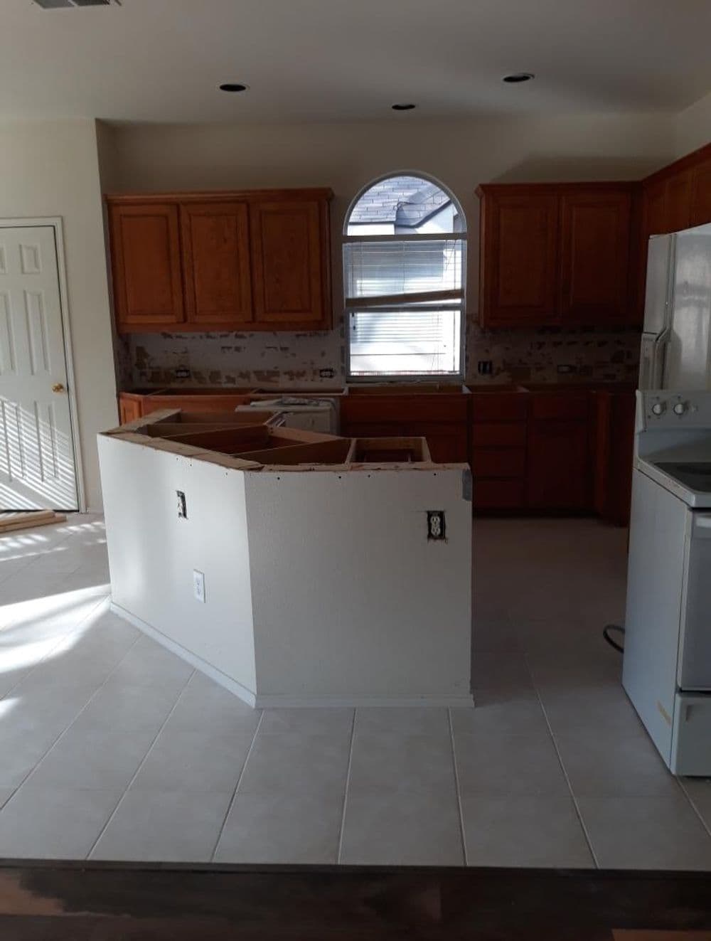 Empty kitchen with wooden cabinets, unfinished counter, and bright natural light through window.