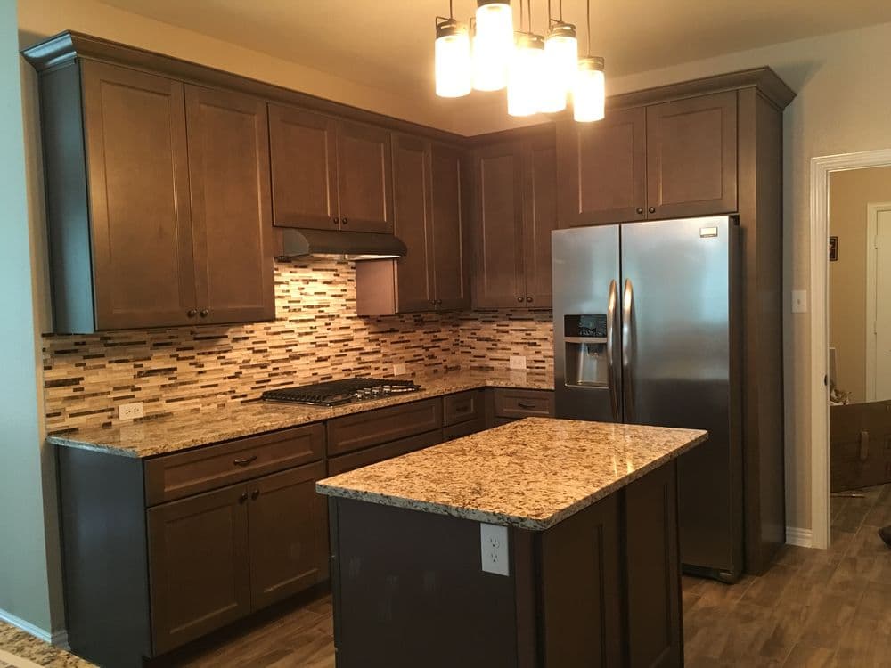 Modern kitchen with dark wood cabinets, stainless steel fridge, and granite island countertop.