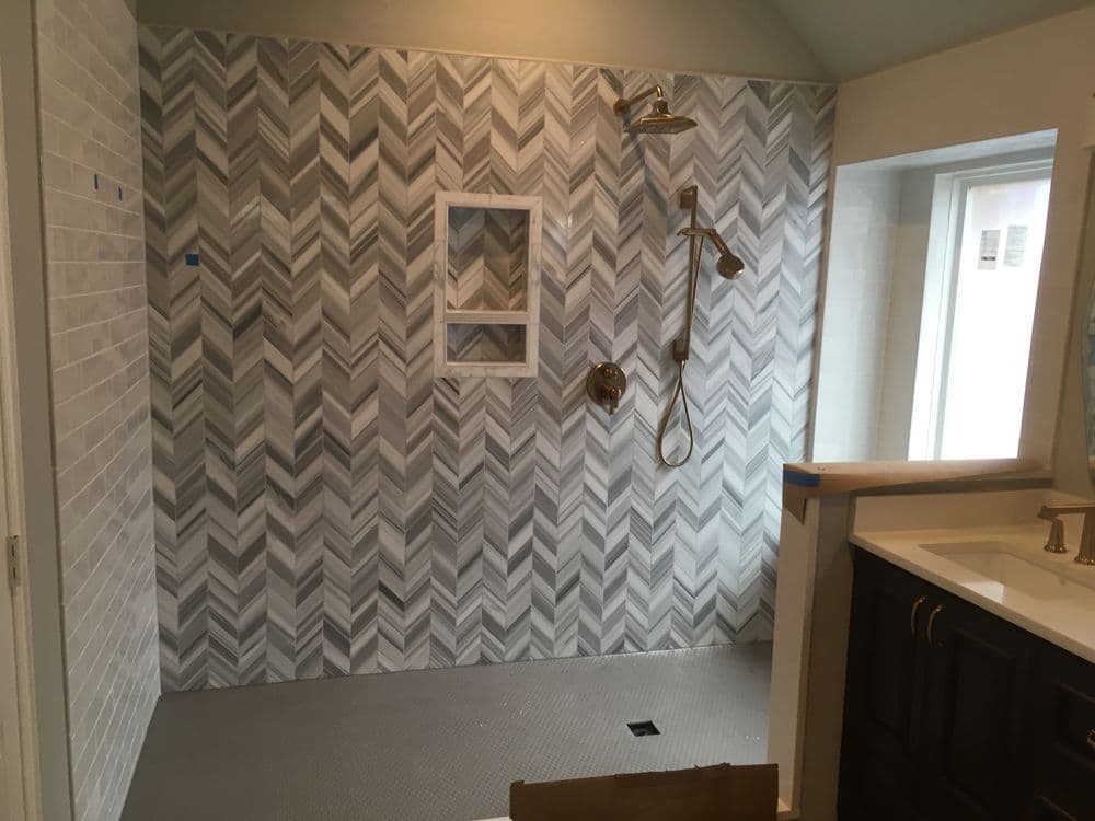 Modern bathroom with herringbone tile shower, gold fixtures, and spacious design.