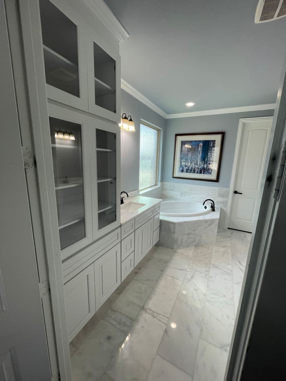 Luxury bathroom with marble floor, modern vanity, and soaking tub under natural light.