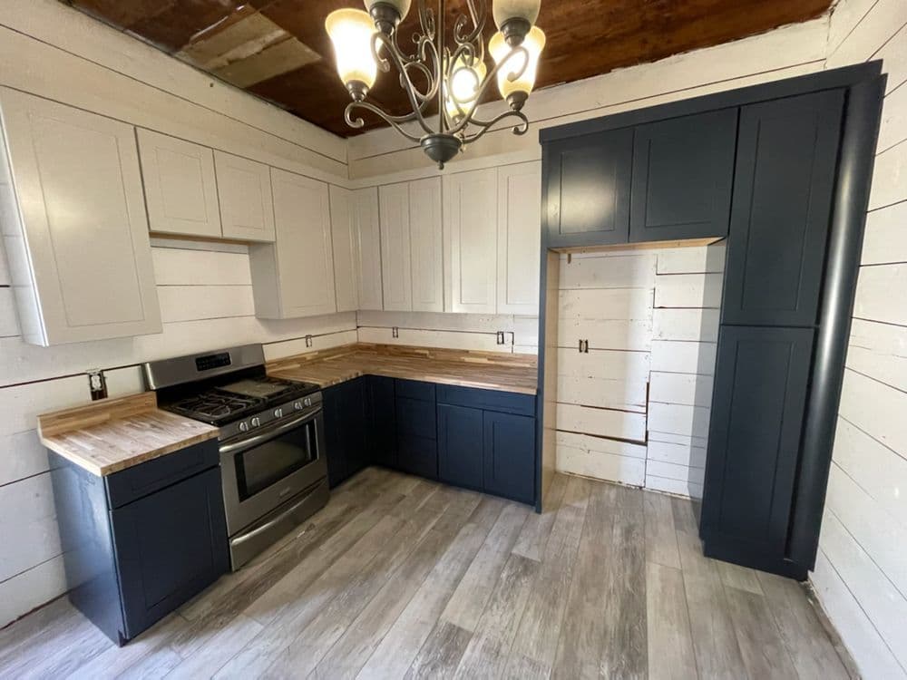Modern kitchen with dark blue cabinets, wood countertops, and stainless steel stove in rustic setting.