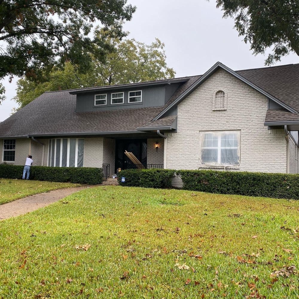 Modern brick home with a manicured lawn, featuring large windows and a dark roof.