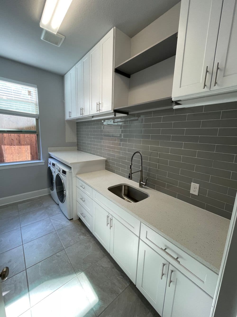 Modern laundry room with white cabinets, gray tile backsplash, and washer/dryer setup.