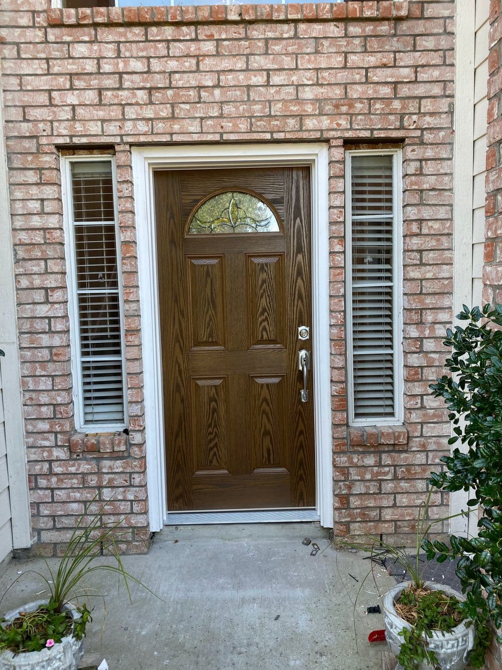 Brown front door with decorative glass, flanked by windows and potted plants at entryway.
