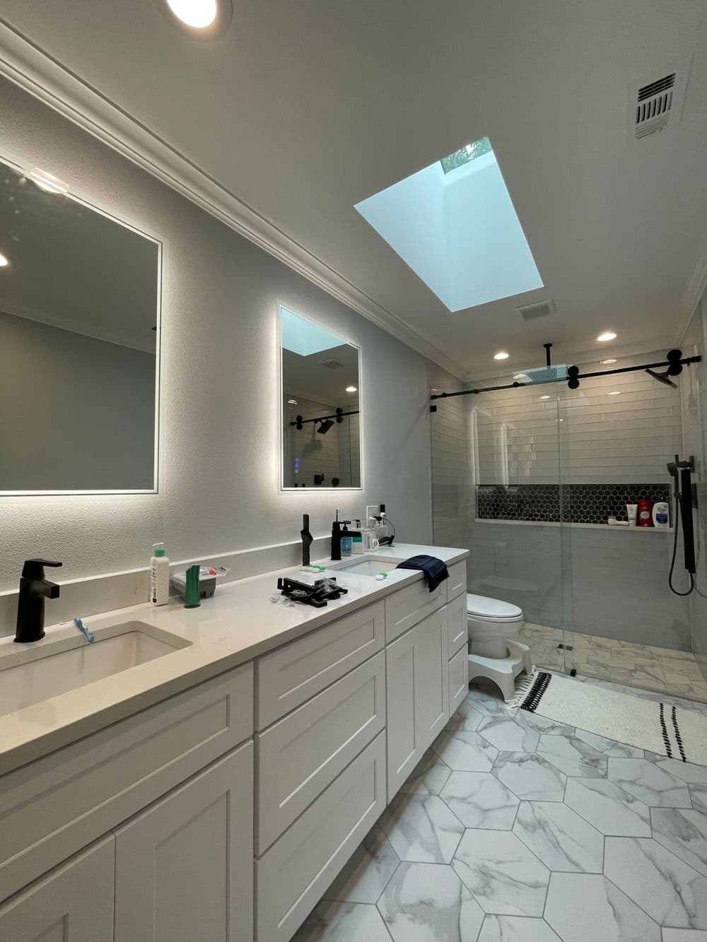 Modern bathroom with dual sinks, large shower, skylight, and elegant stone tiles.