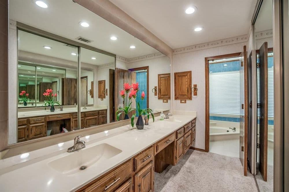 Spacious bathroom with dual sinks, wooden cabinets, and floral decor, featuring a large mirror.