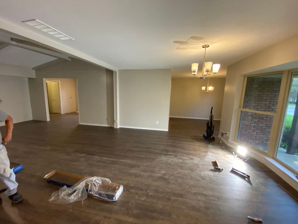Spacious living room with hardwood floors, chandelier, and large windows in a renovated home.
