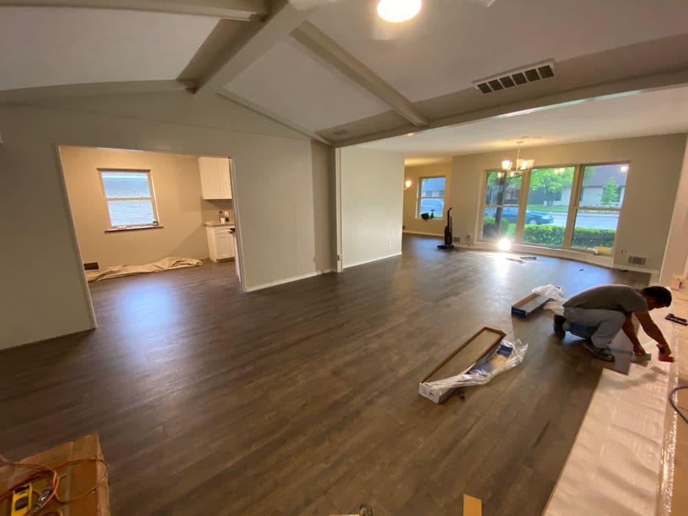 Living room renovation with new flooring and an open layout, showing kitchen in the background.
