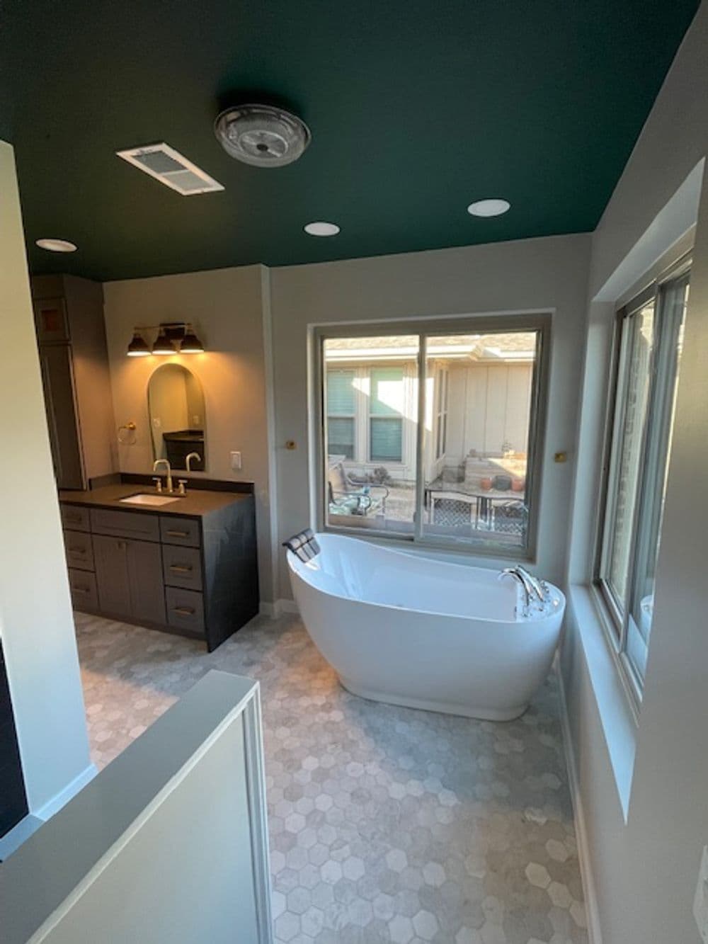 Modern bathroom featuring a freestanding tub, dark cabinetry, and large windows for natural light.