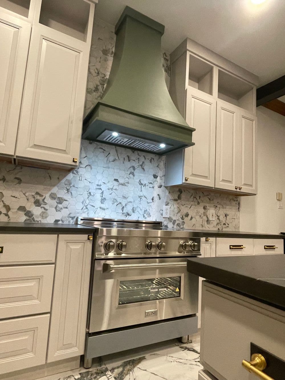 Modern kitchen with gray cabinetry, marble backsplash, and a ZLINE stove under a green hood.