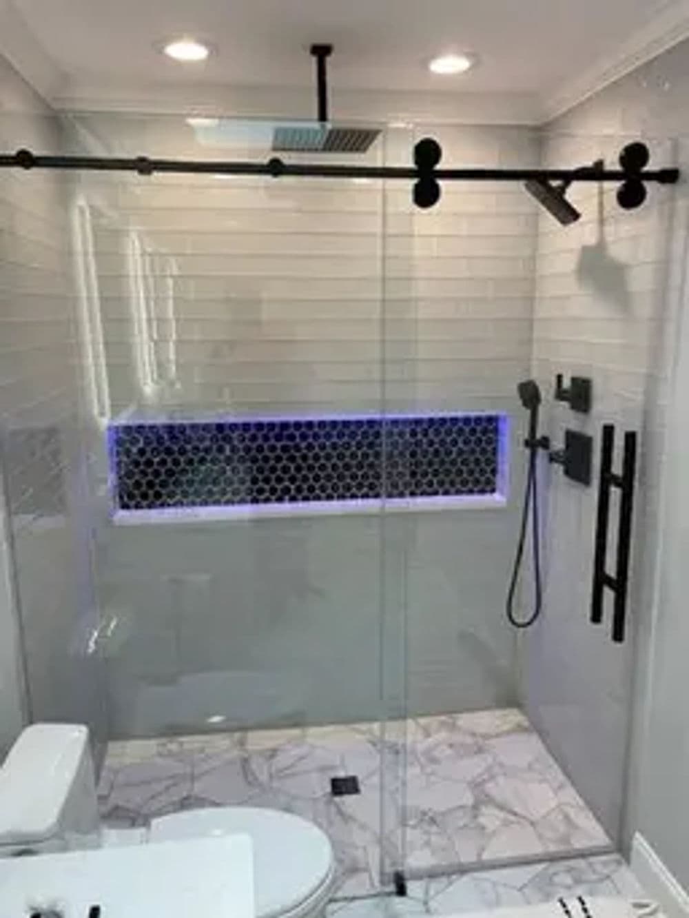 Modern bathroom with glass shower, unique lighting, and stylish tile design.