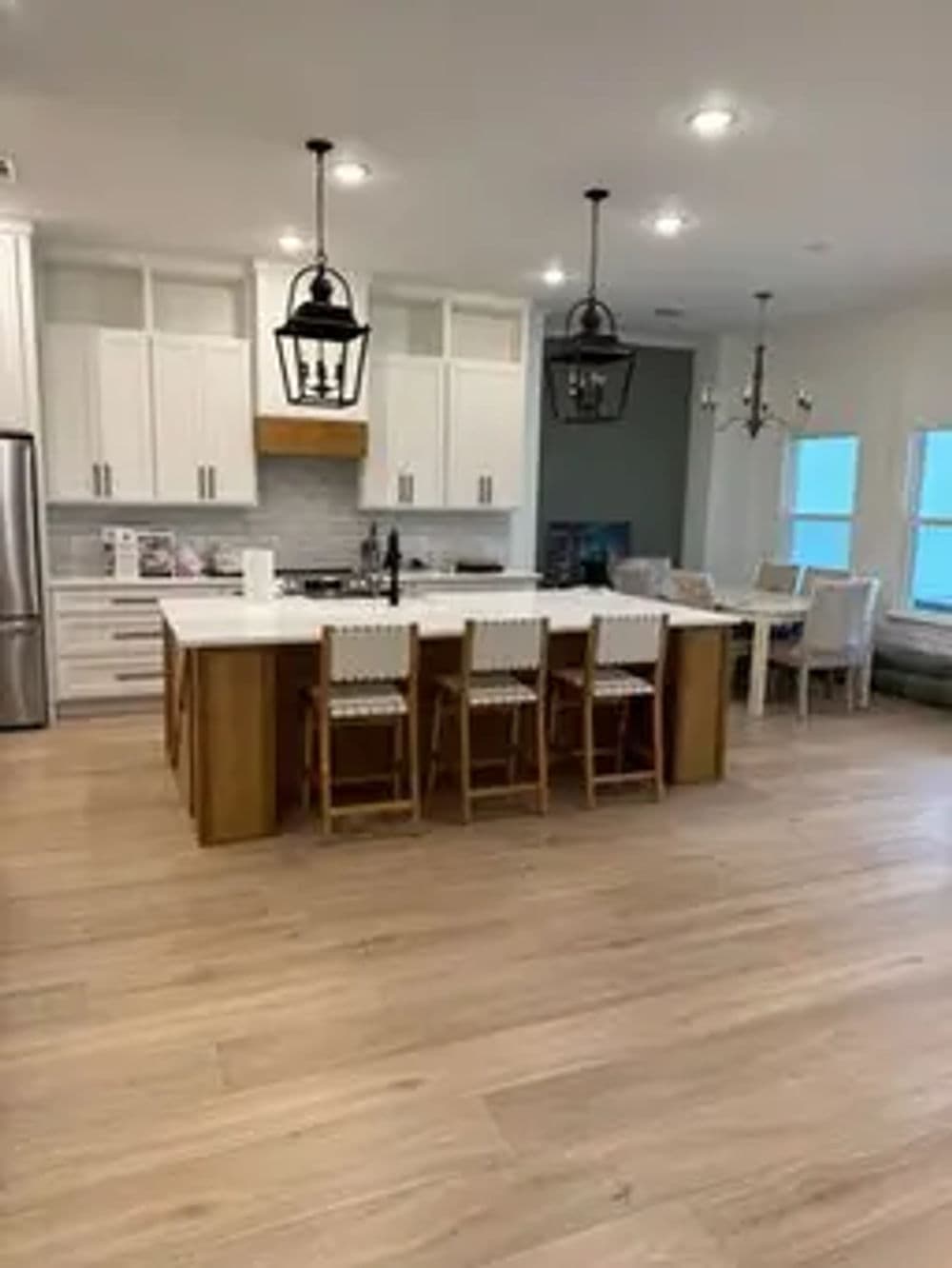 Modern kitchen with wooden flooring, island seating, and pendant lights. Bright and spacious design.