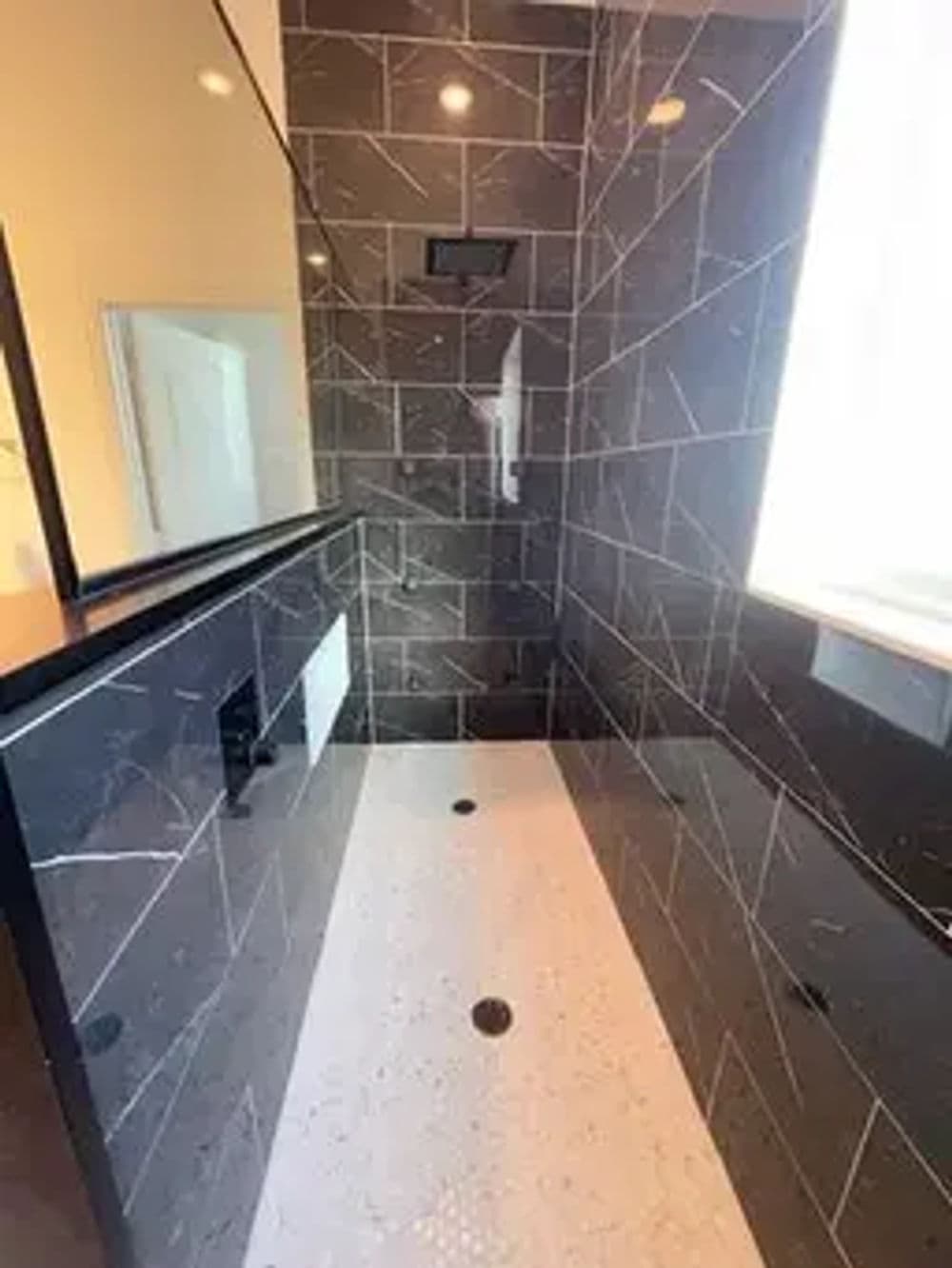 Modern black marble shower design with large window and sleek fixtures. Minimalist style.