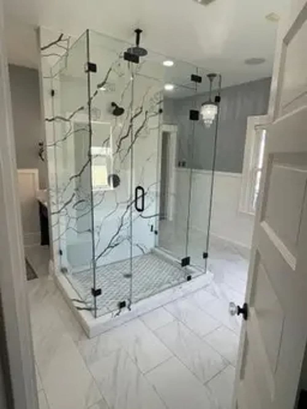 Modern glass shower with black fixtures and marble tile in elegant bathroom setting.