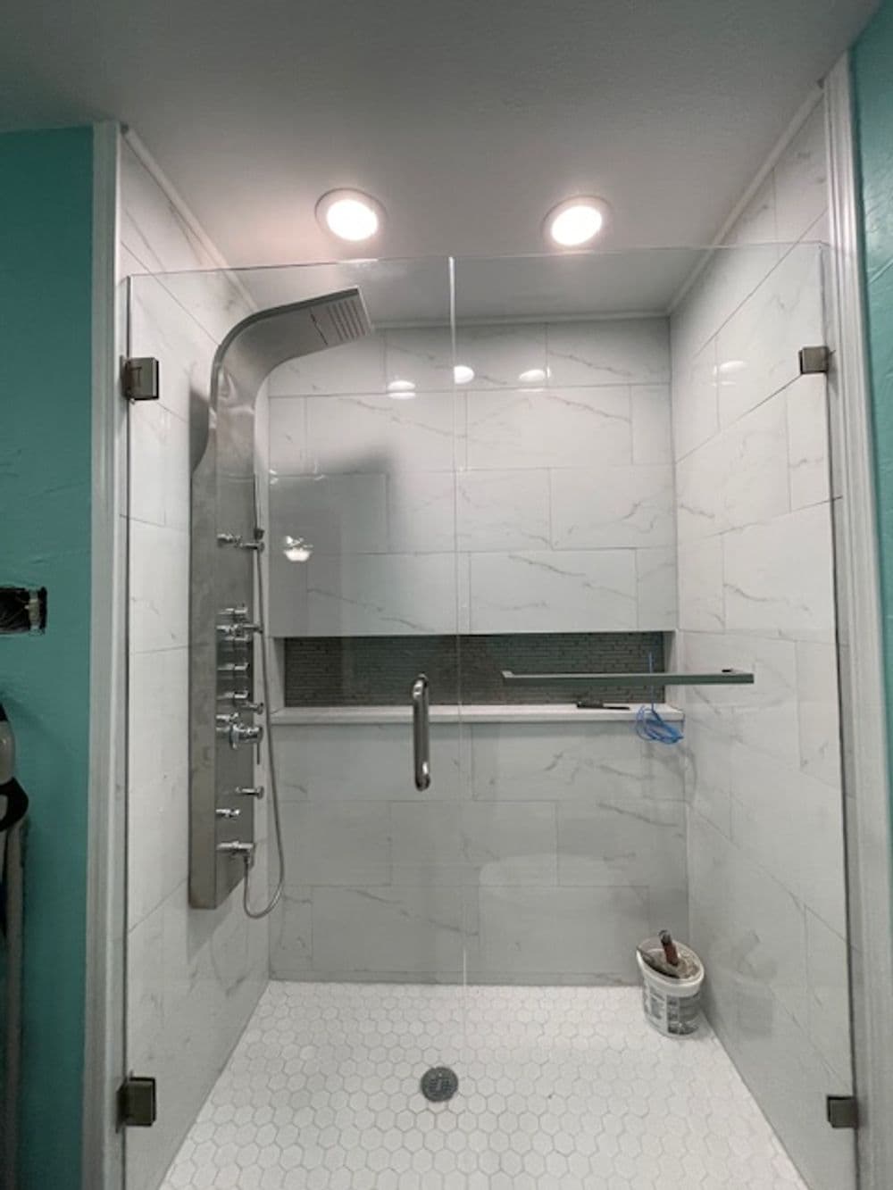 Modern shower enclosure with glass walls, rain showerhead, and hexagonal tile flooring.
