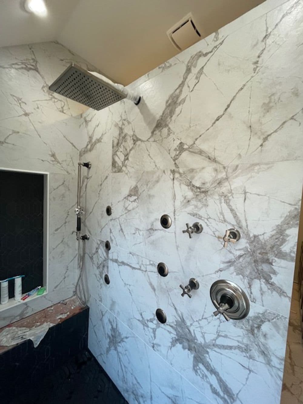 Modern shower with marble walls, rain showerhead, and multiple water control valves.