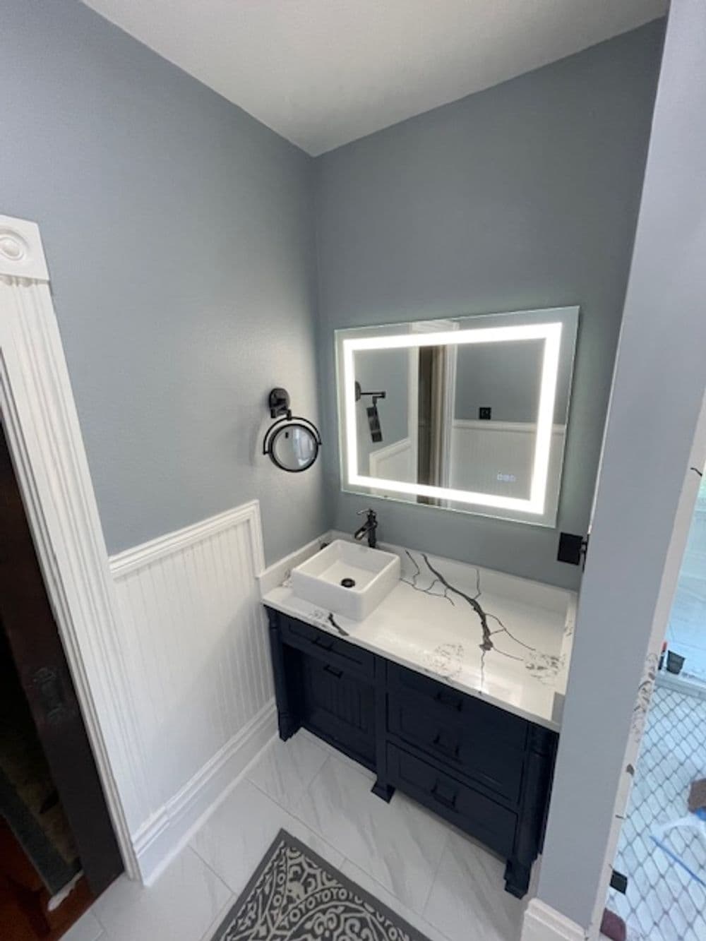 Modern bathroom with a sleek black vanity, illuminated mirror, and elegant marble countertop.