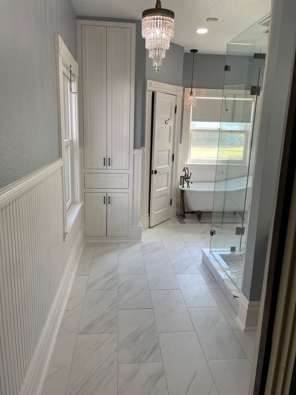 Stylish bathroom interior with marble floor, glass shower, and elegant lighting fixtures.