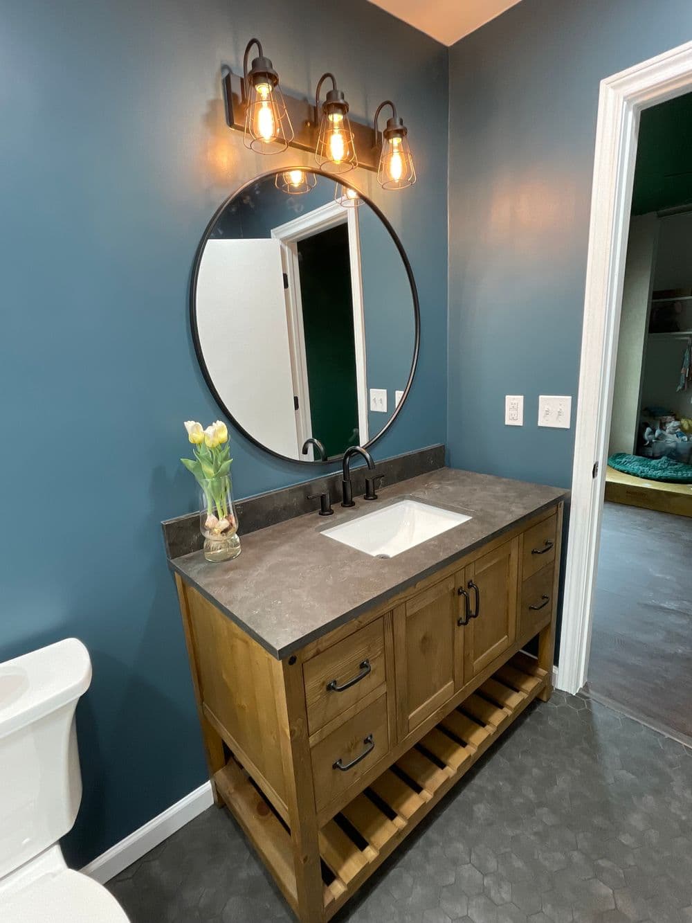 Modern bathroom with a round mirror, industrial lighting, and wooden vanity with countertop sink.