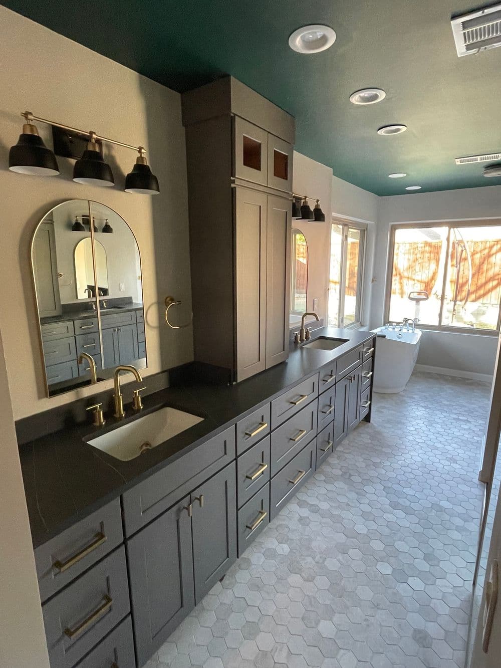 Modern bathroom design featuring dark cabinetry, gold fixtures, and hexagon tile flooring.