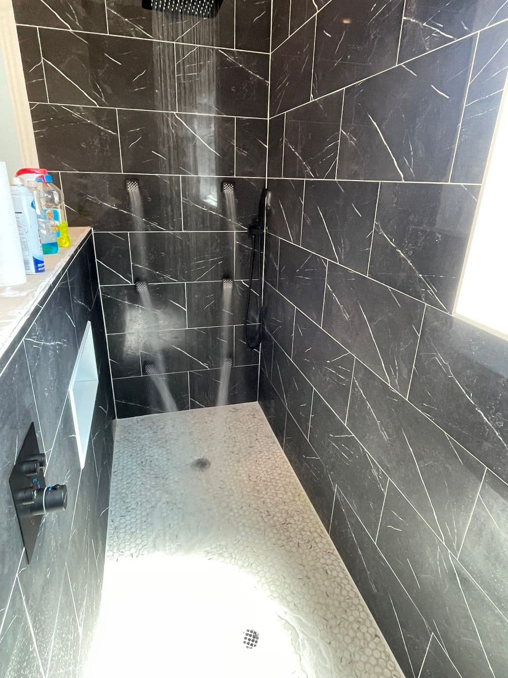 Modern shower with black slate tiles and pebble stone floor, featuring a rainfall showerhead.