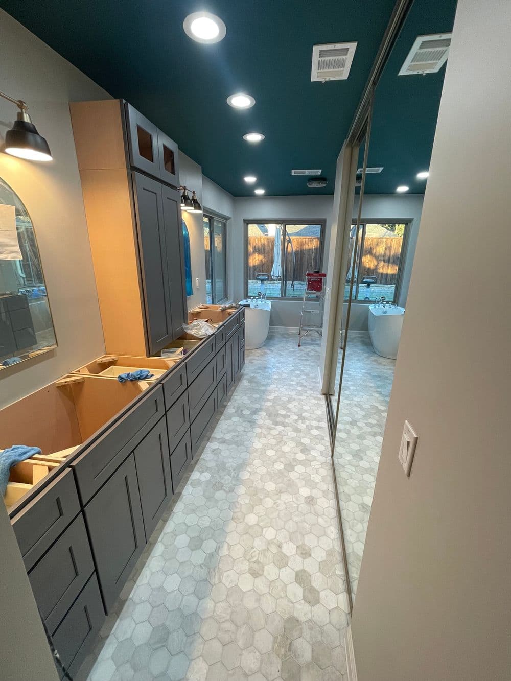 Modern bathroom renovation in progress with gray cabinetry, hexagon tiles, and natural lighting.