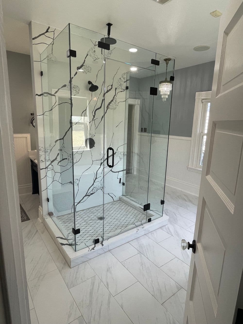 Modern marble tiled bathroom featuring a spacious glass shower enclosure with sleek black hardware.