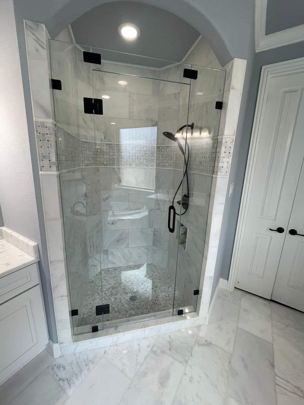 Modern glass shower enclosure with marble walls and floor, featuring elegant black hardware.