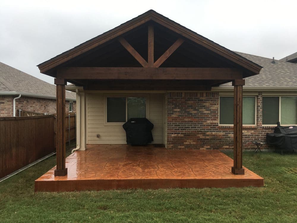 New wooden patio cover with a stone-stamped concrete floor in a backyard setting.