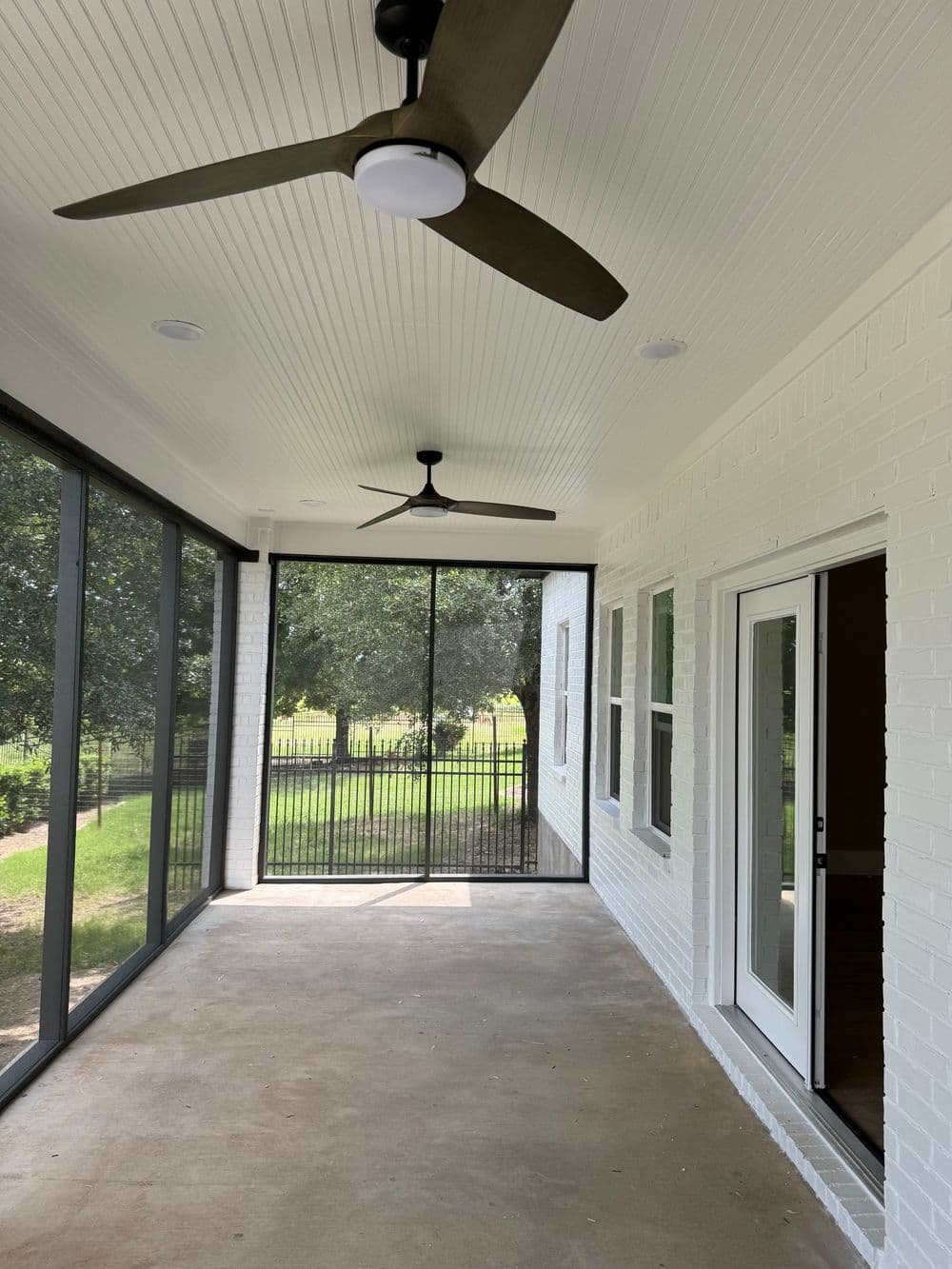Spacious screened-in porch with ceiling fans and white brick walls, overlooking a green yard.