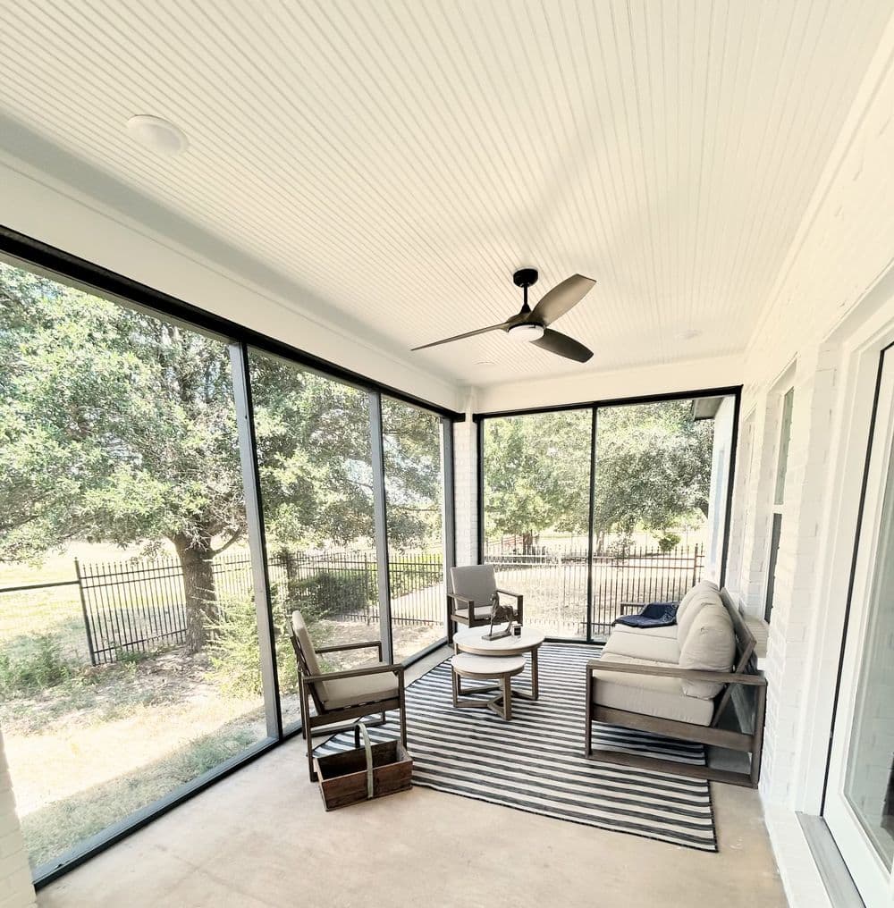 Spacious screened porch with modern furniture, ceiling fan, and scenic outdoor view.