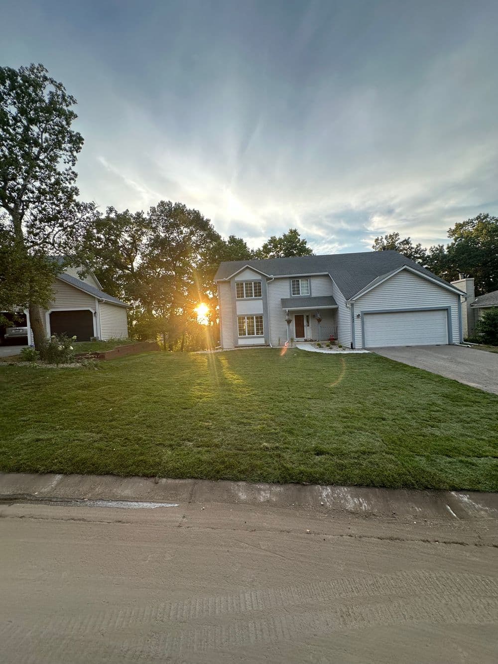 Sunset view of a suburban home with freshly mowed lawn and nearby trees.